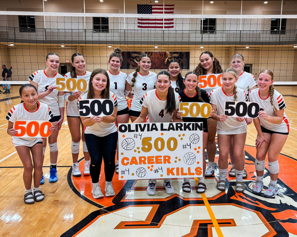 Members of the Black River Falls High School volleyball team pose together on the court, surrounding junior Olivia Larkin, who holds a handmade sign reading "Olivia Larkin 500 Career Kills." The teammates smile while holding cutouts of the number "500" to celebrate her milestone.