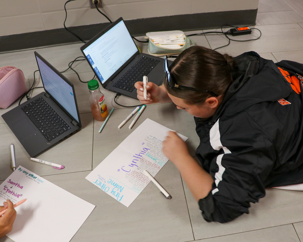 A group of students collaborating on the floor, writing key phrases and drawing illustrations on a bright poster board.