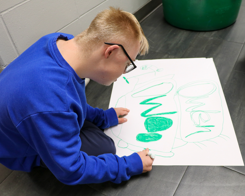 A student sitting on the floor, using markers to trace letters on a poster board during a group project session.