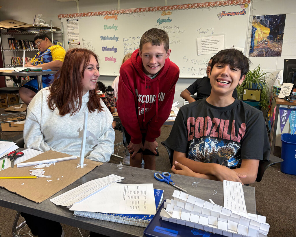 Three students smile at a table.