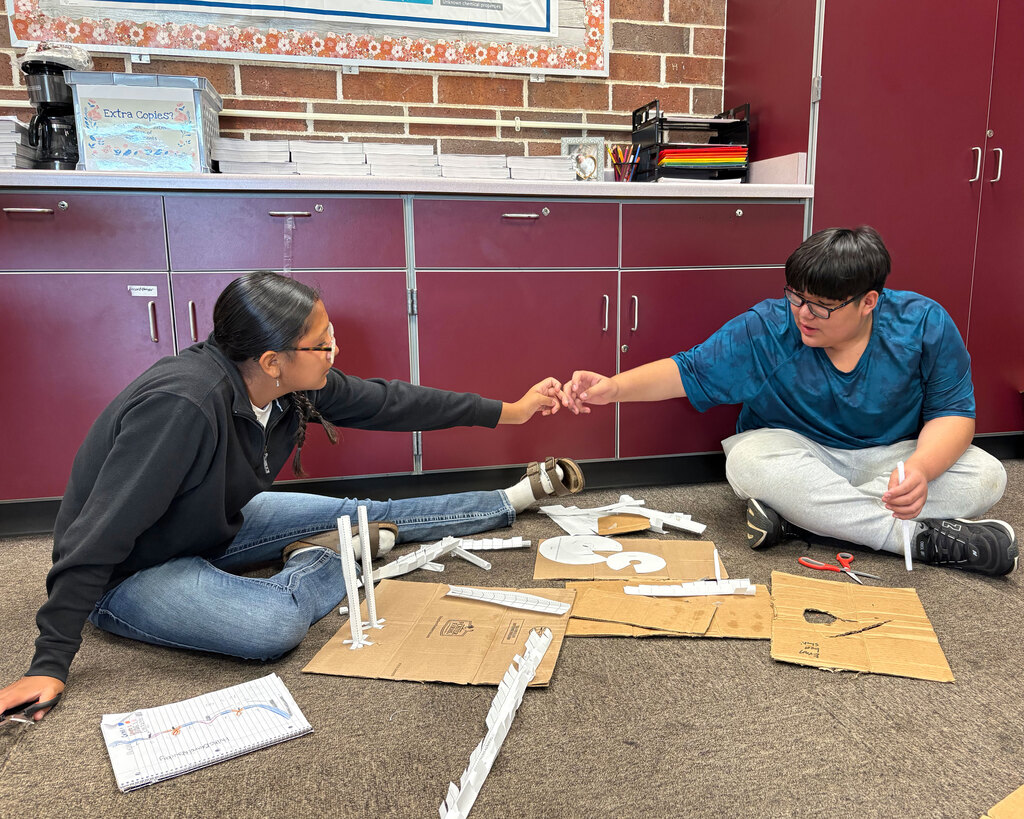 Two middle school students sit together on the carpeted classroom floor,