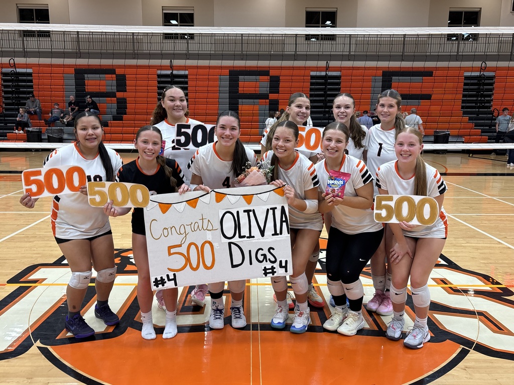 Photo of a group of voleyball players holding a sign that says Congrats Olivia. 500 Digs.