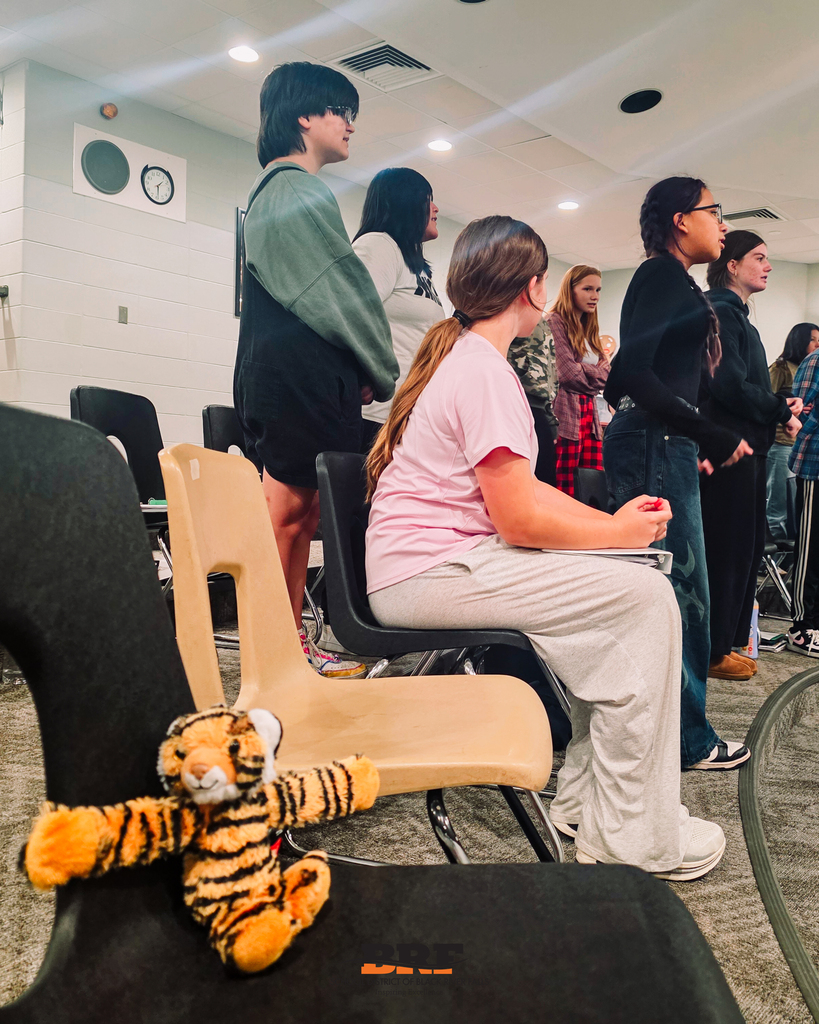 Students sing in choir while a stuffed tiger sits in a chair