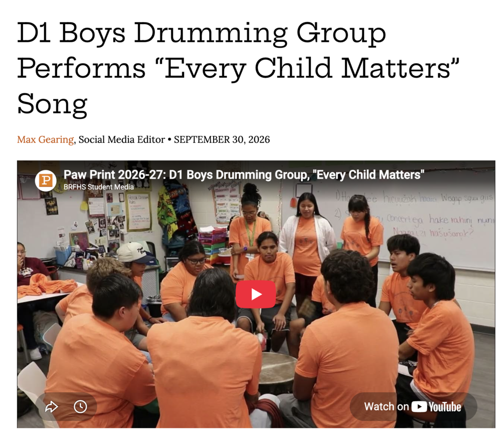 A group of students wearing matching orange shirts sitting in a circle indoors around a central drum, with standing onlookers watching, under the article headline "D1 Boys Drumming Group Performs 'Every Child Matters' Song."