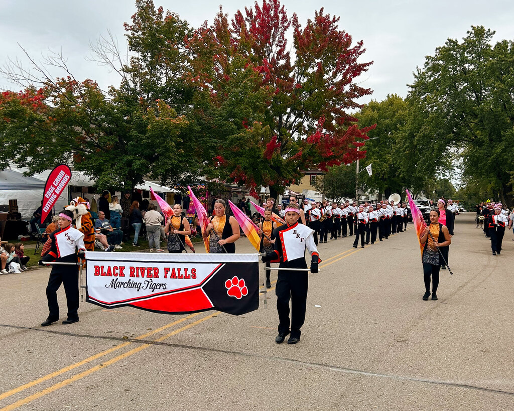 The Black River Falls Marching Tigers marching in a parade on a street lined with trees showing autumn colors.