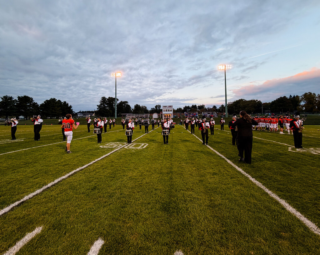 The Black River Falls Marching Tigers lined up in formation across a football field at dusk during a pregame performance.