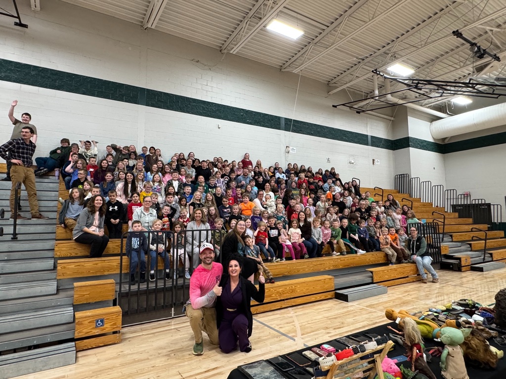 Ed the Diver and Christie B pose in front of a large group of Florence Elementary students seated in the gym bleachers. Students and staff are smiling and gathered for a group photo.