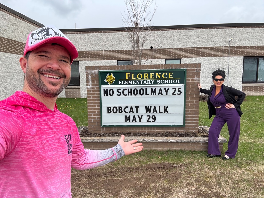 Ed the Diver and Christie B pose outside Florence Elementary School near the school sign, smiling and gesturing toward it.