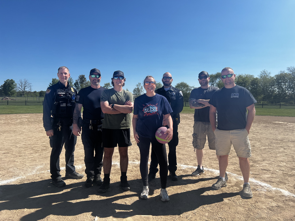 Group of cops that played kickball with the students.  Wearing sunglasses and one is holding a kickball on a baseball field infield