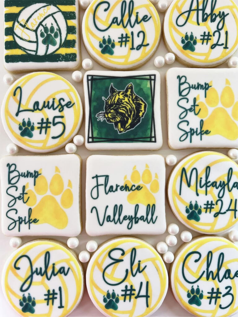 Flat-lay view of custom decorated sugar cookies celebrating a volleyball team, featuring player names, jersey numbers, volleyballs, wildcat mascot logos, and terms like "Bump Set Spike" and "Florence Volleyball" in green and yellow icing.