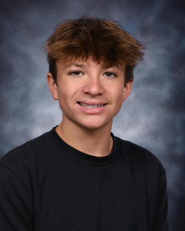 A school portrait of a teenage boy with messy light brown hair, smiling gently while wearing a black long-sleeved shirt against a textured, dark cloudy blue background.