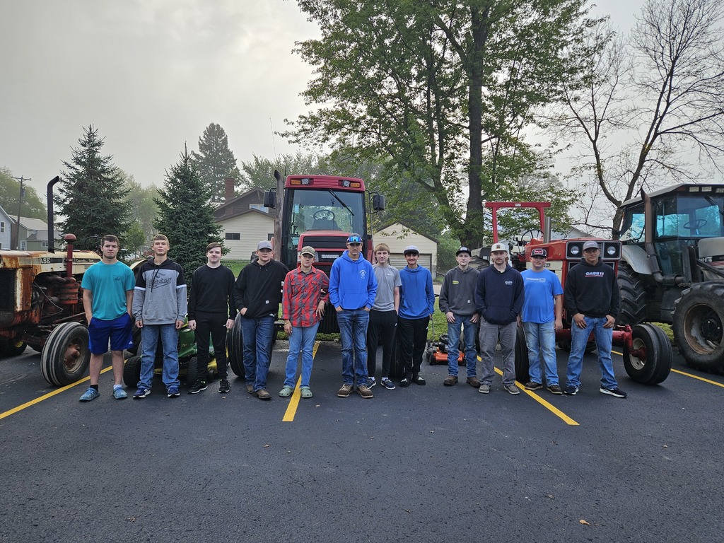 Tractors parked in a row, trees in the background, students standing in front of parked tractors