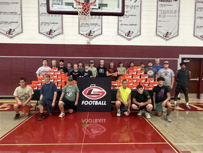 gymnasium with football players lined up with 55 pairs of shoe boxes stacked in pyramids