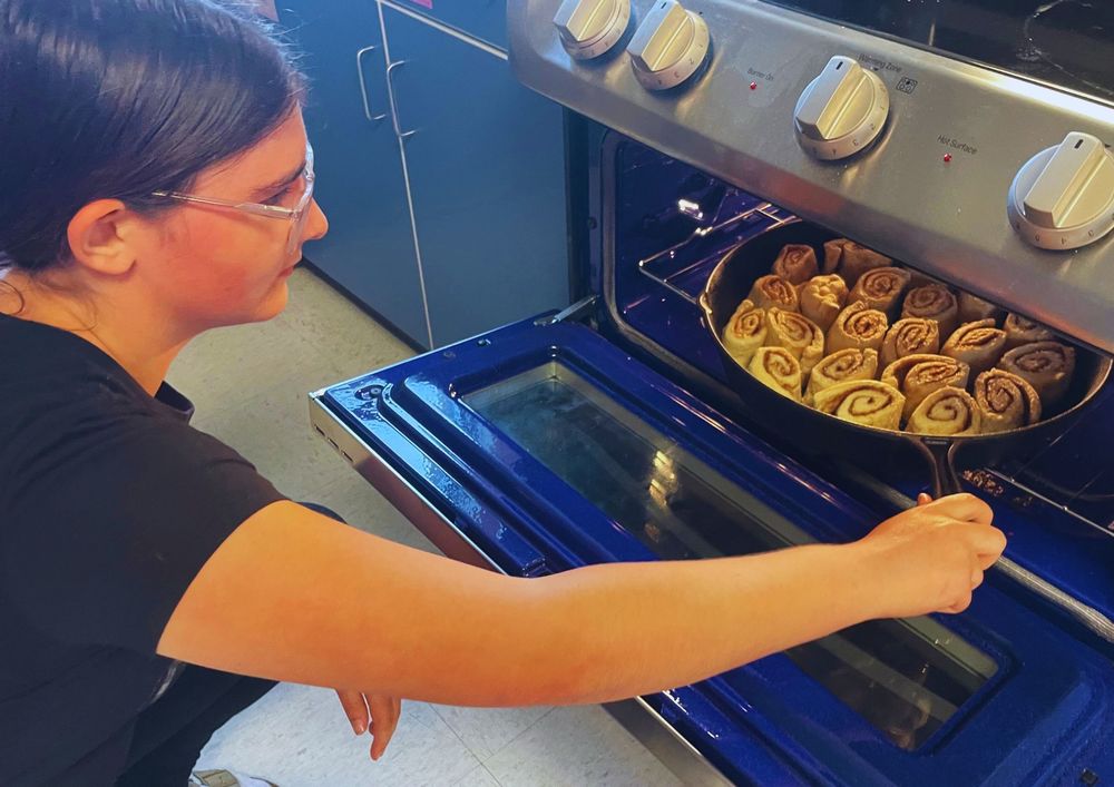 Student puts cinnamon rolls into oven
