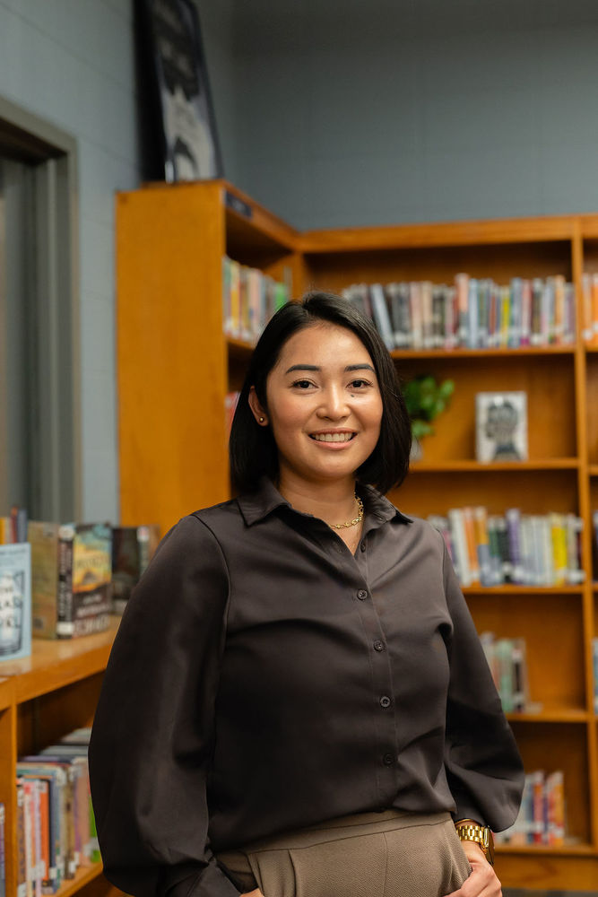 Gem Elmer poses for a portrait in the MS/HS library with books in the background.