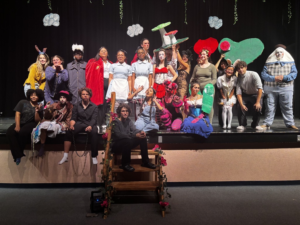 A cast of a student production seated on a stage for a group photo.