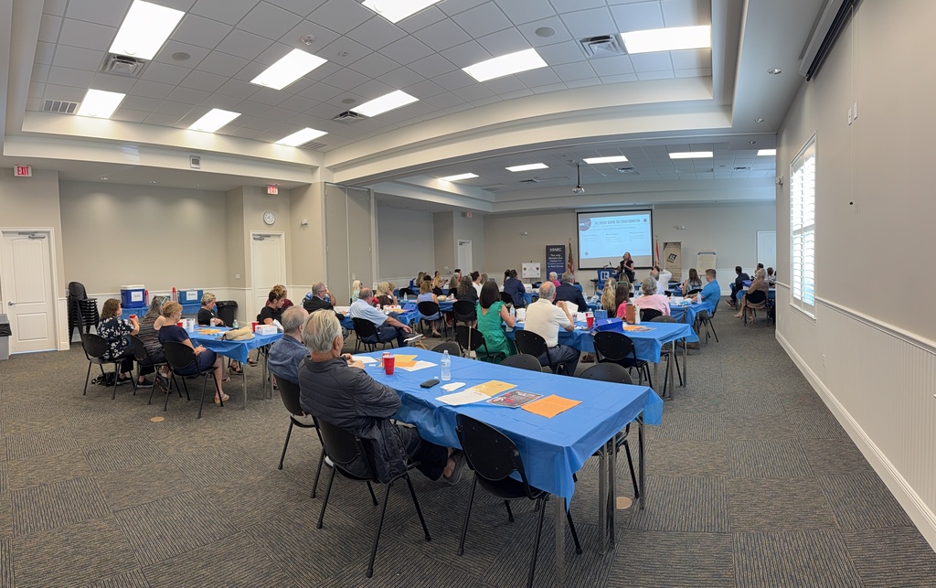 A room filled with community members and local real estate professionals attending a presentation by Dr. Christina Jacobs of the School District of Indian River County. Attendees listen from tables throughout the meeting space as Dr. Jacobs speaks at the front of the room.