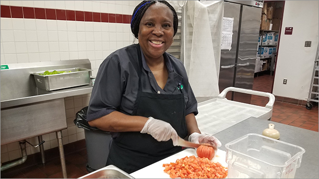 smiling food service worker slices vegetables in the school cafeteria kitchen