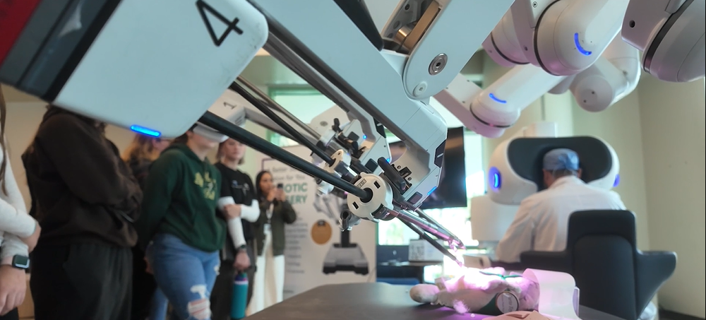 a surgical robot operating on a small plush with students looking on