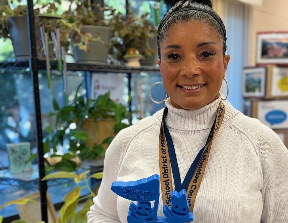 Teacher holding a bright blue and green trophy.
