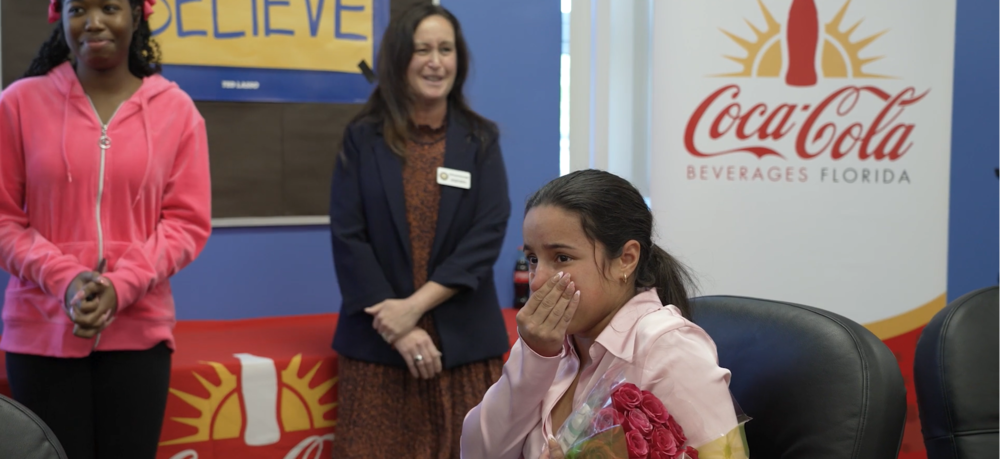 A young woman holds her hand over her mouth in surprise as she holds a dozen roses.