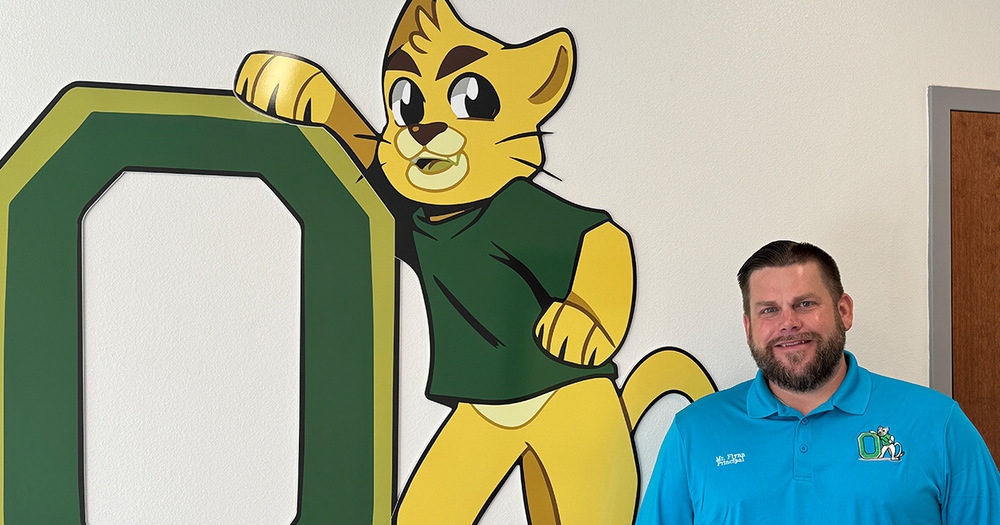 School principal standing next to a wall with the Oneco Elementary mascot painted on it.