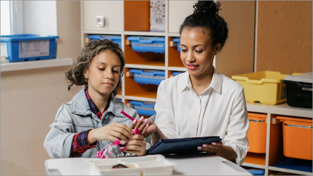 young paraprofessional helps student in the classroom