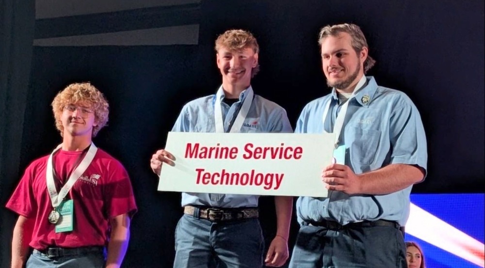 Two men wearing blue shirts holding a sign which reads 'Marine Service Technology'