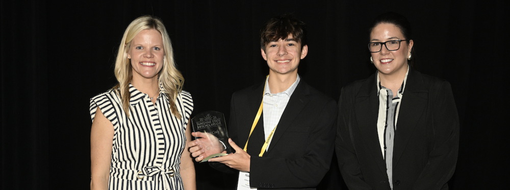 Two educators with a teenaged student holding a glass trophy.