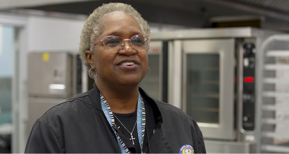 A smiling cafeteria worker wearing glasses and hoop earrings.