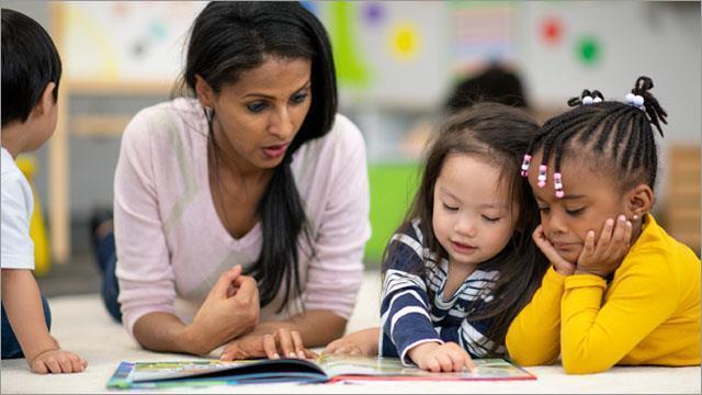 small children and their teacher read a book together in the classroom