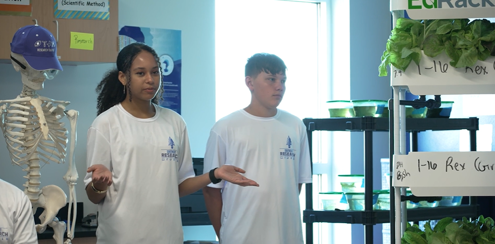 Students presenting a research project in a classroom next to a hydroponics system.
