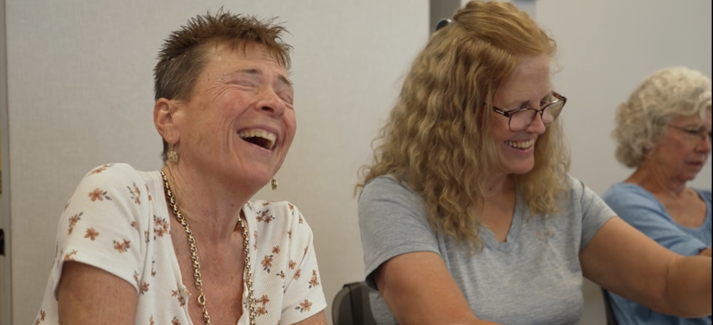 Two ladies laughing and smiling while sitting down at a table