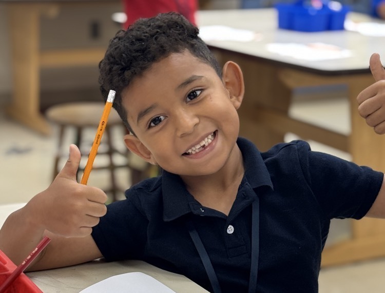 A boy holding a pencil with one hand and a thumbs up in the other