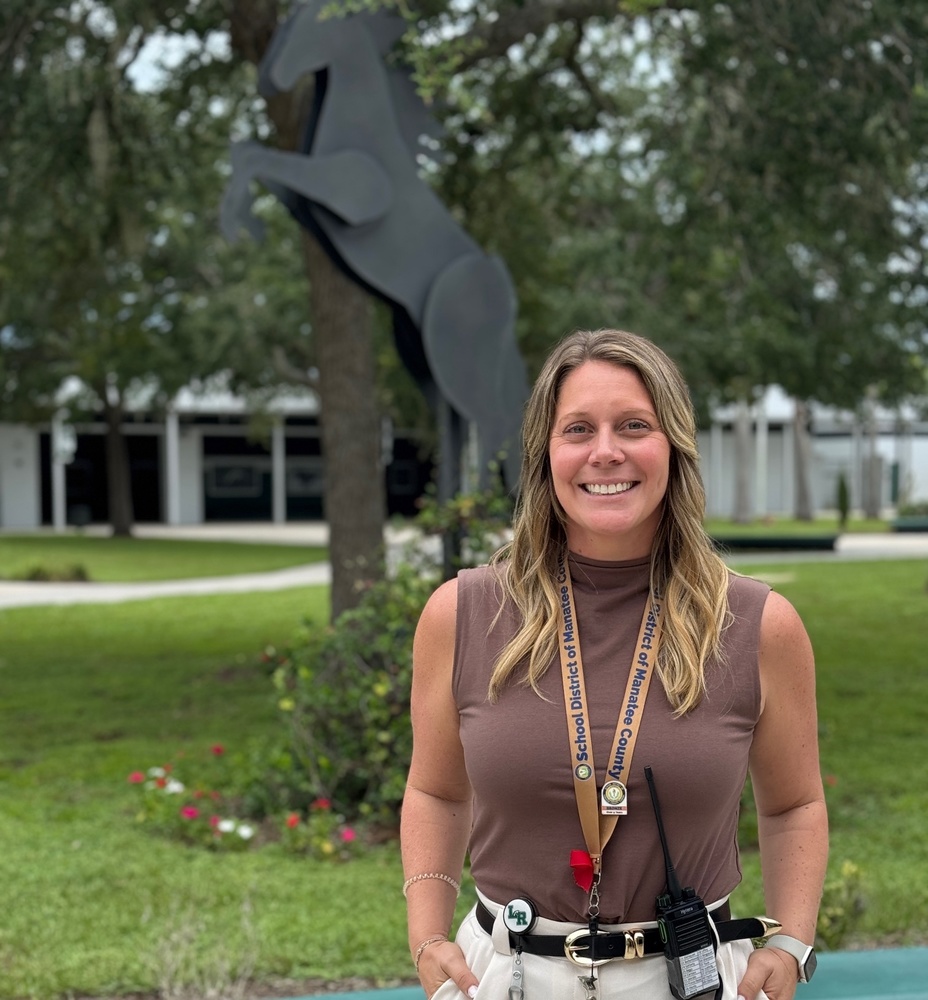 A school administrator smiling in front of a sculpture - the school mascot, a Mustang