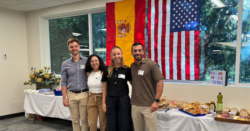 Four teachers standing in front of a table of food and in front of an American and Spain flags