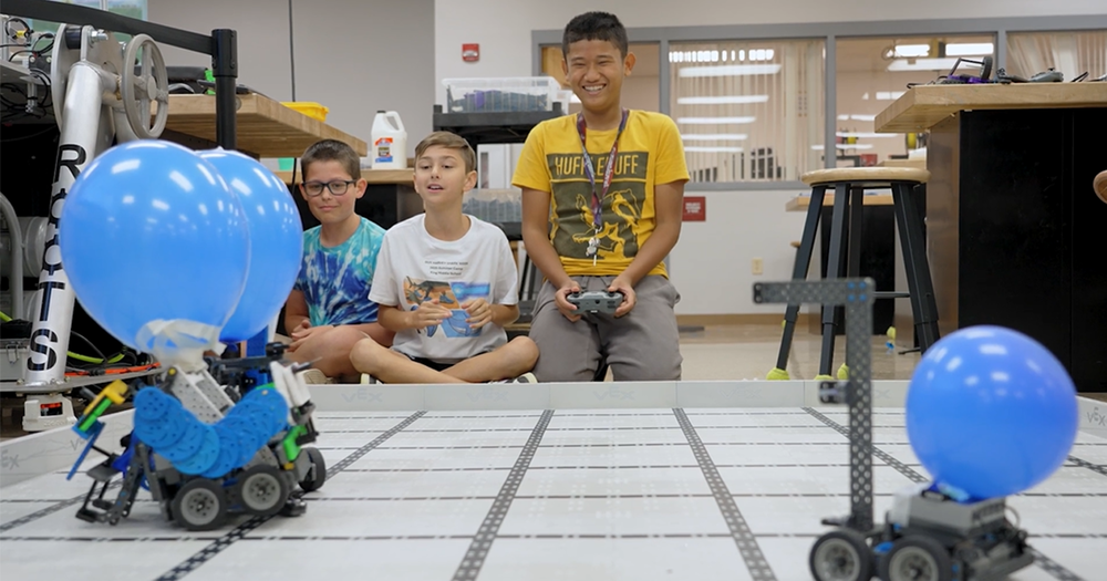 Students smiling and using controllers to drive robots.