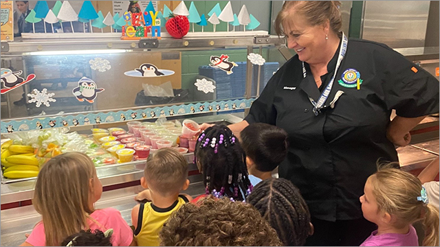 cafeteria manager helps students with their lunch selections