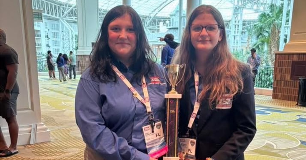 Two teens holding a gold trophy in a hotel conference center in Nashville.