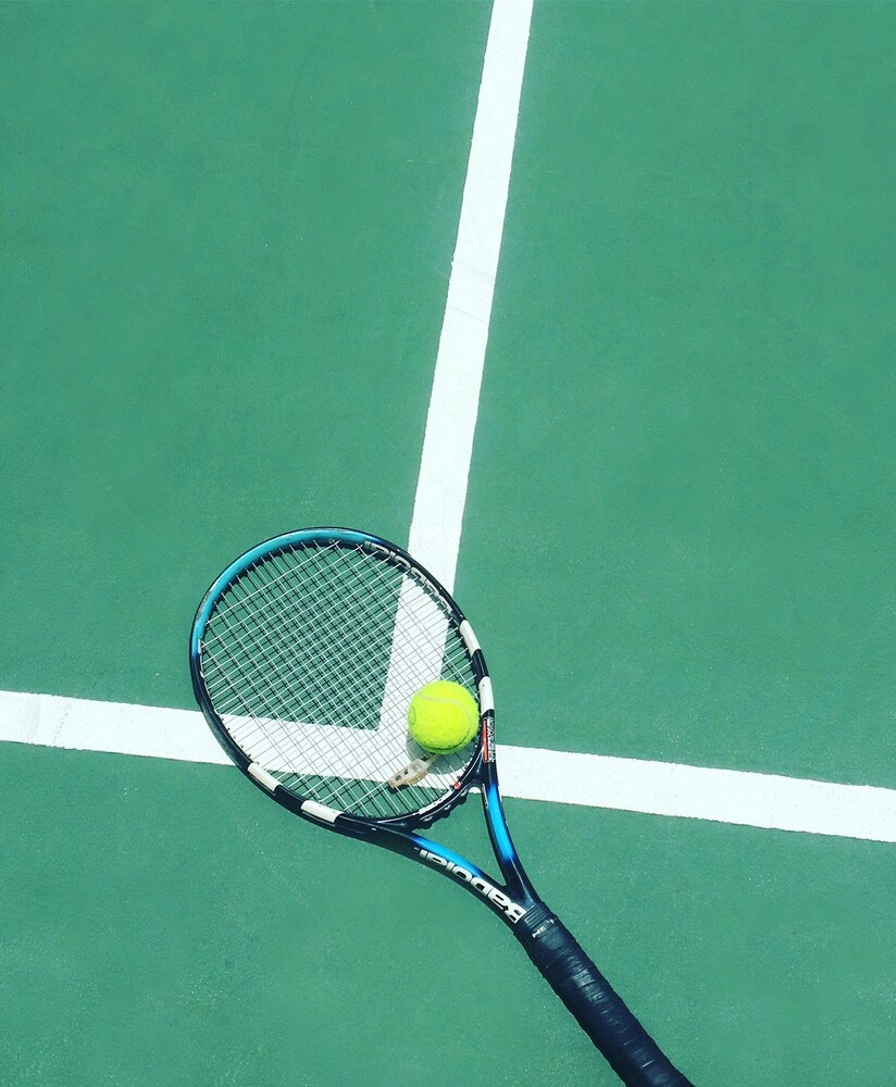 Tennis court in the background with a tennis racket and ball. 