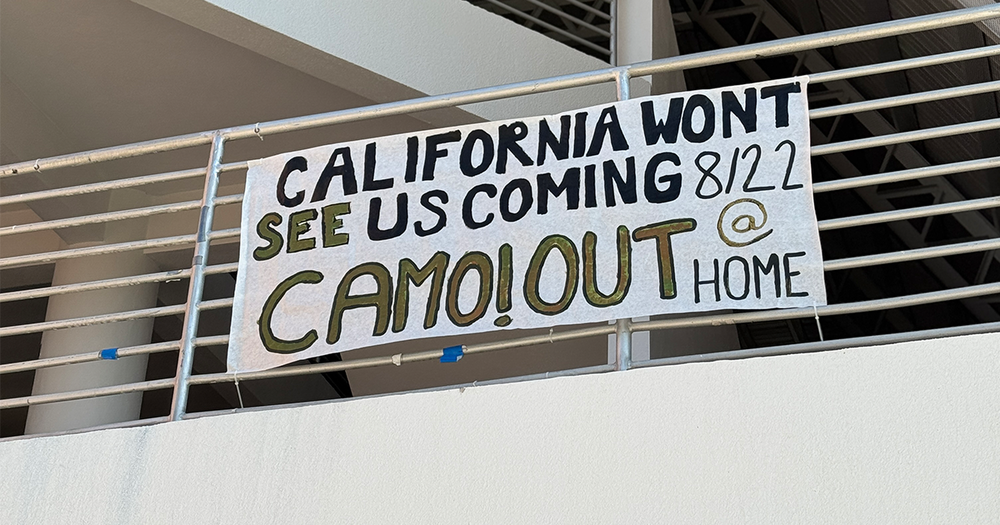 A sign that reads "California won't see us coming 8/22 Camo! Out at Home"