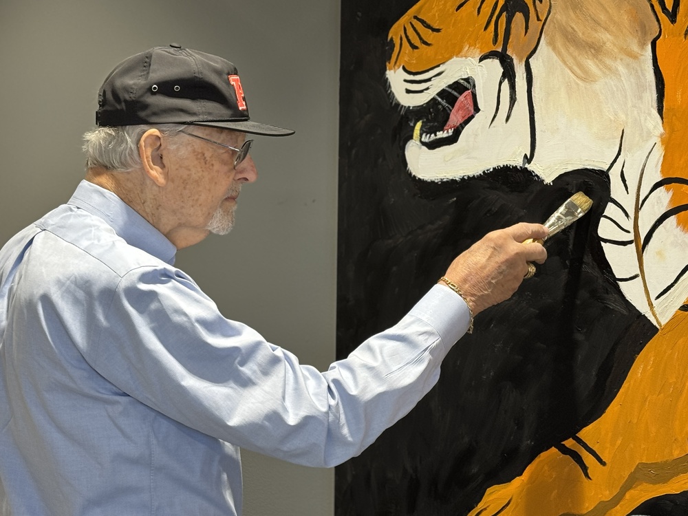 A man paints a tiger mural on the wall.