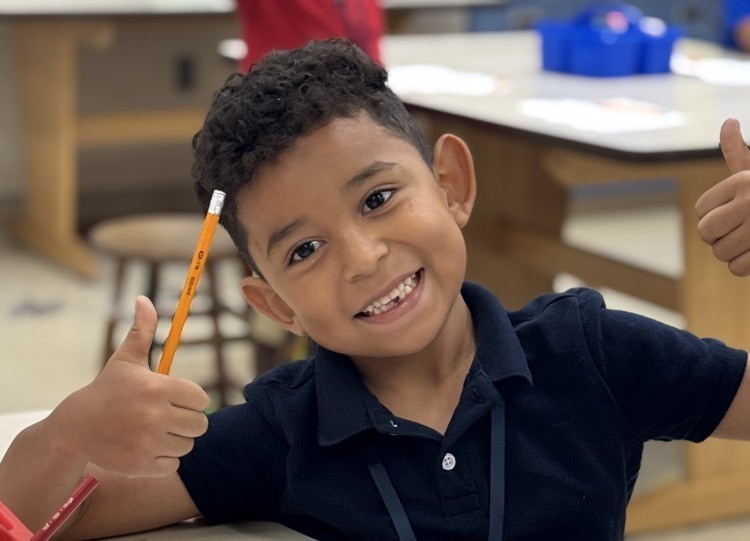 A boy holding a pencil in one hand and a thumbs up in the other