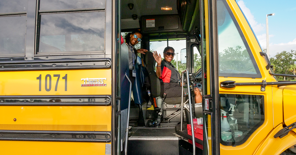 A school bus driver and aide wave from inside the bus on the first day of school