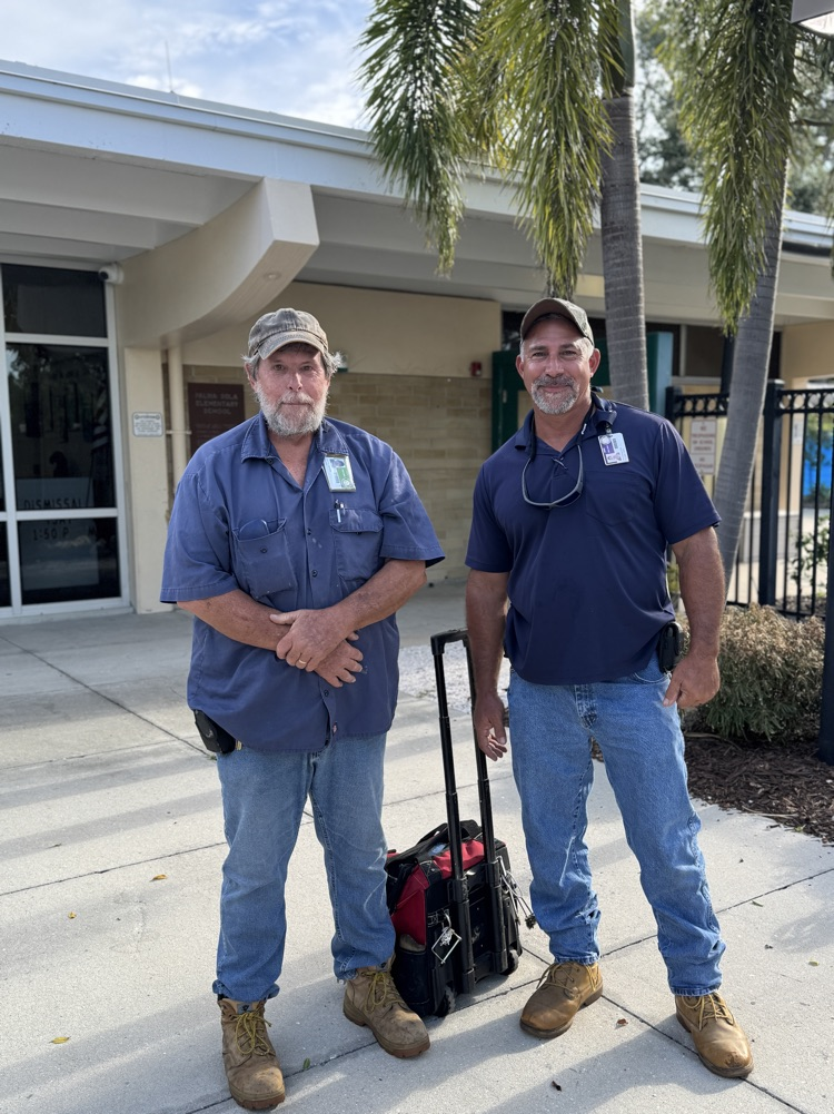 two men wearing blue shirts, jeans, and boots at a school working to fix a plumbing issue.