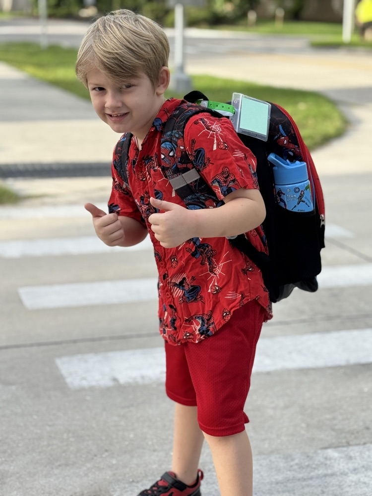 A boy wearing red gives a thumbs up while walking to school