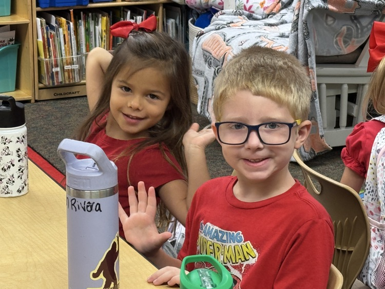 Two children wearing red waves to the camera