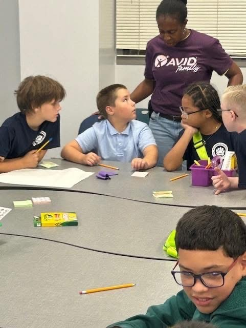 Students smile around a table inside a classroom