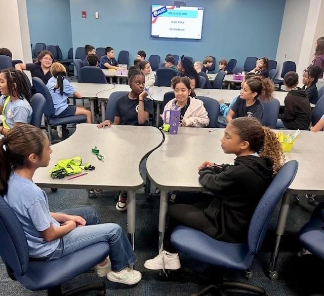 Student sitting around a large table discussing their assignment