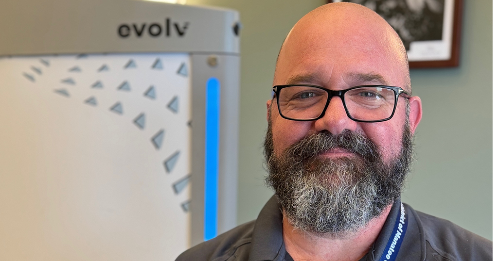 A smiling, bearded safety guardian wearing glasses while standing next to an evolv machine.